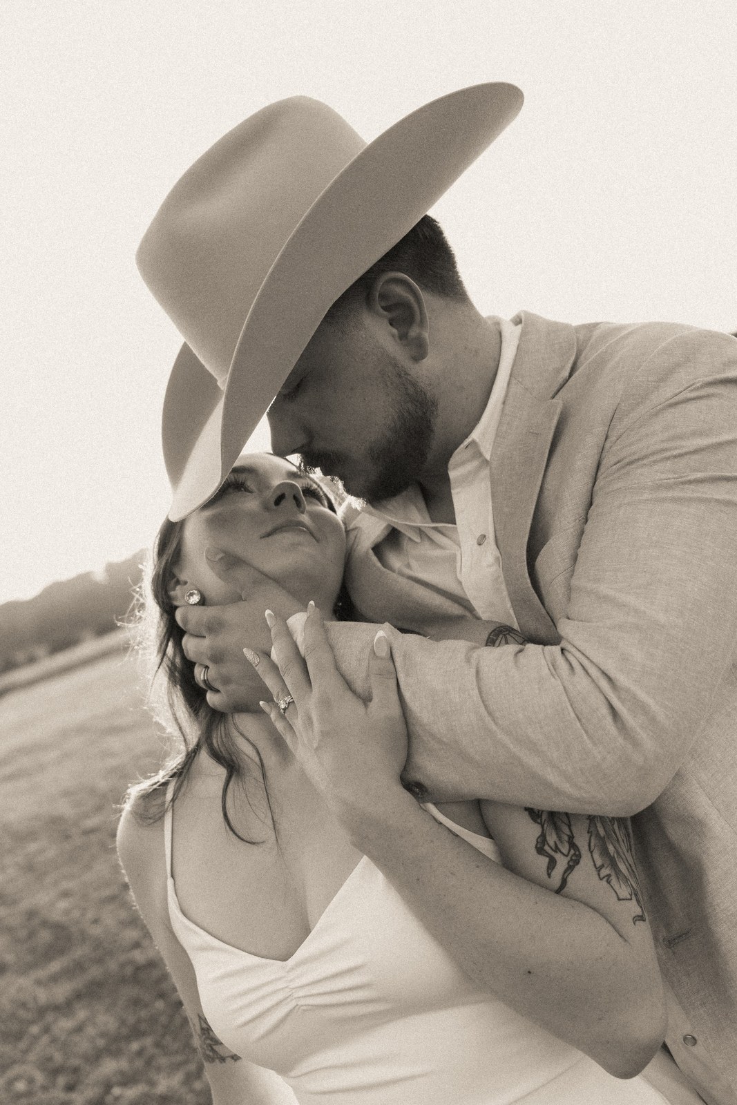 Black-and-white image of a bride and groom kissing behind a hat